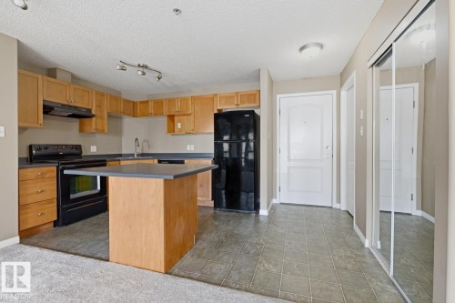 Kitchen area with wood-finish cabinetry, dark countertops, and black appliances - 5106 7335 South Terwillegar Drive, Edmonton, AB - Indoor Photo Showing Kitchen