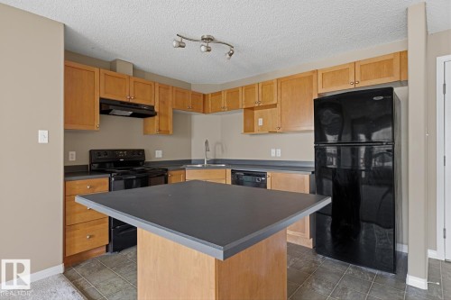 Kitchen featuring light wood cabinetry, dark countertops, black appliances, a central island, and tile flooring - 5106 7335 South Terwillegar Drive, Edmonton, AB - Indoor Photo Showing Kitchen