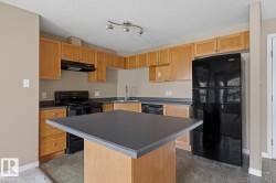 Kitchen featuring light wood cabinetry, dark countertops, black appliances, a central island, and tile flooring - 