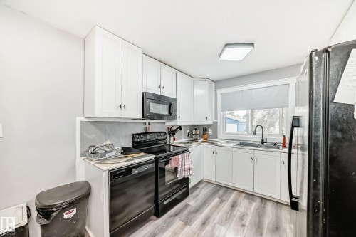 Kitchen featuring white cabinetry, black appliances, a double basin sink with a matte black faucet, light wood-finish flooring, and a large window - 3802 52 Street, Wetaskiwin, AB 