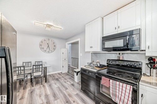 Kitchen featuring white cabinetry with black hardware, wood-finish flooring, a stainless steel refrigerator, and black appliances - 3802 52 Street, Wetaskiwin, AB 