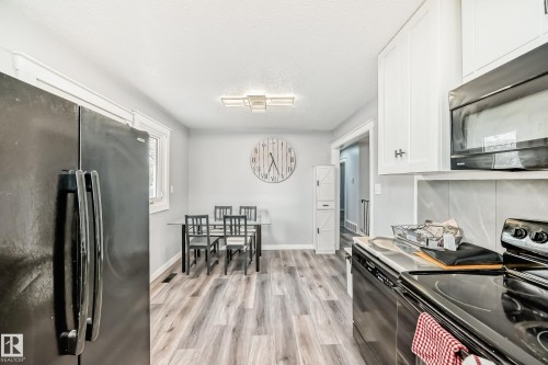 Kitchen featuring wood-finish flooring, white cabinetry with dark hardware, a built-in microwave, and a black electric range - 3802 52 Street, Wetaskiwin, AB 