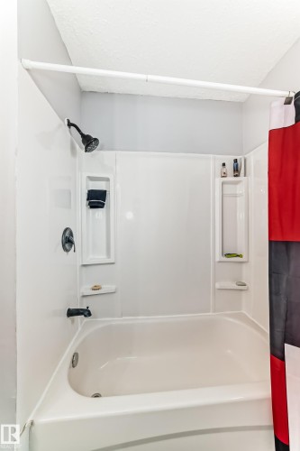 White tub and shower combination featuring a matte black shower head, coordinating faucet, and built-in shelving - 3802 52 Street, Wetaskiwin, AB 