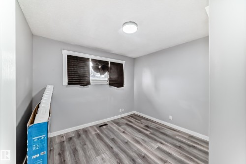 Neutral-toned room featuring wood-finish flooring, a window with horizontal blinds, and a flush-mount ceiling light fixture - 3802 52 Street, Wetaskiwin, AB 