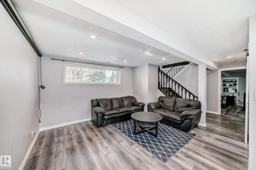 Spacious lower-level area featuring wood-finish flooring, a large window, recessed lighting, and a staircase with dark wood railings - 3802 52 Street, Wetaskiwin, AB 