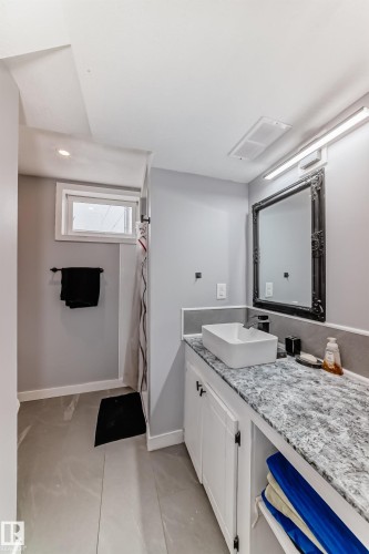 Bathroom featuring a rectangular vessel sink, stone-finish countertop, white cabinetry with black hardware, and an ornate framed mirror - 3802 52 Street, Wetaskiwin, AB 