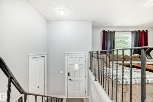 Multi-level interior featuring a decorative wrought iron railing, vaulted ceiling, and a paneled entry door with frosted glass insert - 3802 52 Street, Wetaskiwin, AB 