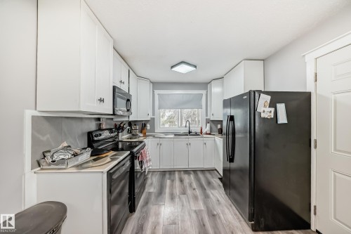 Kitchen featuring white cabinetry, wood-finish flooring, a stainless steel sink with a black pull-down faucet, and a contemporary flush-mount ceiling light fixture - 3802 52 Street, Wetaskiwin, AB 
