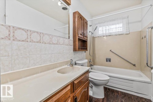 Bathroom featuring a single-basin vanity with an integrated countertop, wood-finish cabinetry, and a full-width mirror - 24 Elizabeth Drive, Fort Saskatchewan, AB - Indoor Photo Showing Bathroom