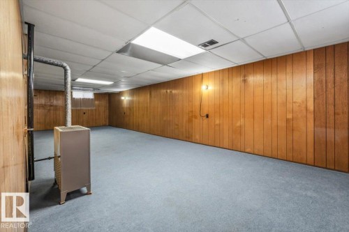 Spacious room with wood paneling, light blue carpeting, and a drop ceiling with integrated lighting - 24 Elizabeth Drive, Fort Saskatchewan, AB - Indoor