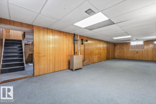 Spacious lower-level room featuring wood-panel walls, light blue carpeting, and a drop ceiling with recessed lighting - 24 Elizabeth Drive, Fort Saskatchewan, AB - Indoor Photo Showing Basement