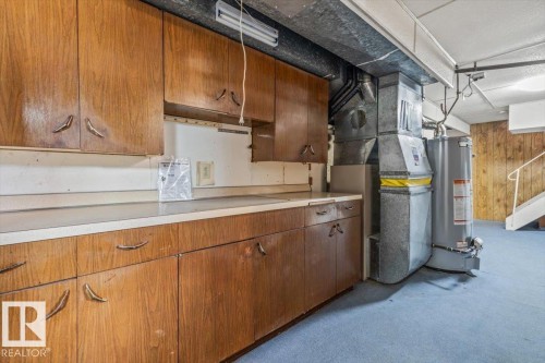 Wood-finish cabinetry with unique hardware, light-toned countertop, exposed ductwork, water heater, and light blue carpeting - 24 Elizabeth Drive, Fort Saskatchewan, AB - Indoor Photo Showing Basement