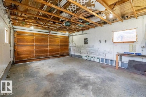 Garage interior featuring an exposed wood beam ceiling, concrete flooring, a wood-finish garage door, a window, and a built-in workbench - 24 Elizabeth Drive, Fort Saskatchewan, AB - Indoor Photo Showing Garage