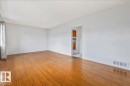Spacious room featuring wood-finish flooring, light neutral wall tones, and an open doorway revealing a partial kitchen with wood cabinetry - 24 Elizabeth Drive, Fort Saskatchewan, AB  - Indoor Photo Showing Other Room 