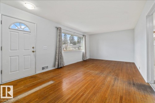 Spacious interior showcasing wood-finish flooring, a multi-pane front entry door with an arched transom, and a wide window with a curtain rod - 24 Elizabeth Drive, Fort Saskatchewan, AB - Indoor Photo Showing Other Room