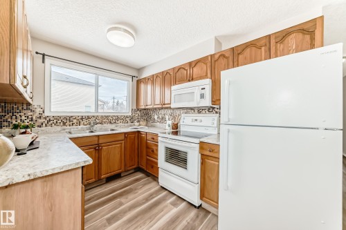 The kitchen features wood cabinetry, a tiled backsplash, and light-colored countertops - 10329 150 Street, Edmonton, AB - Indoor Photo Showing Kitchen