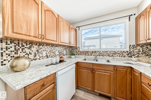 The kitchen features wood cabinetry, light-colored countertops, and a tiled backsplash - 10329 150 Street, Edmonton, AB - Indoor Photo Showing Kitchen With Double Sink