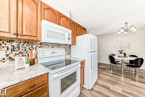 The kitchen features wooden cabinetry, white appliances, a tiled backsplash, and a light-colored countertop - 10329 150 Street, Edmonton, AB - Indoor Photo Showing Kitchen