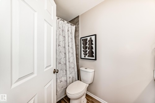 The bathroom features a white toilet, a shower with a patterned curtain, and wood-look flooring - 10329 150 Street, Edmonton, AB - Indoor Photo Showing Bathroom