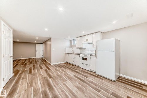 Open concept living area featuring wood-look flooring, recessed lighting, and a kitchen area with white cabinetry, a refrigerator, and a range - 10329 150 Street, Edmonton, AB - Indoor Photo Showing Kitchen