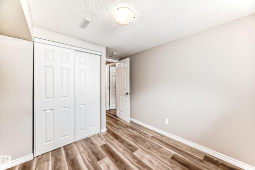 This room features wood-look flooring, light-colored walls, a closet with white paneled sliding doors, and a ceiling light fixture - 10329 150 Street, Edmonton, AB - Indoor Photo Showing Other Room