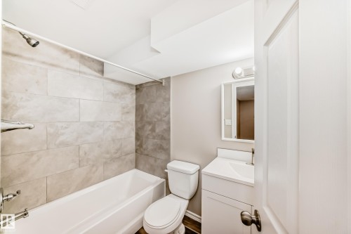 The bathroom features a white bathtub with light-colored tile surround, a toilet, and a vanity with a rectangular sink and a mirror - 10329 150 Street, Edmonton, AB - Indoor Photo Showing Bathroom