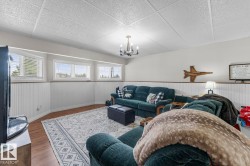 Recreational room featuring wood-finish flooring, white beadboard wainscoting, white walls, and a dropped ceiling with recessed panels - 
