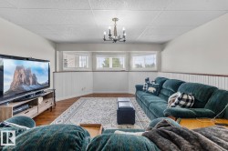 Expansive room featuring wood-finish flooring, white beadboard paneling, and multiple windows with horizontal blinds - 