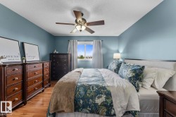 Spacious bedroom featuring wood-finish flooring, a ceiling fan with integrated lighting, and a window with white drapery - 