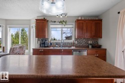 Kitchen featuring a spacious island with a stone-finish countertop, wood cabinetry, and a mosaic tile backsplash - 