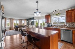 Kitchen featuring a large island with countertop seating, wood-finish flooring, stainless steel appliances, wood cabinetry, and a mosaic tile backsplash - 