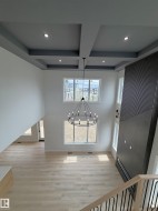 Two Story  living area featuring wood-finish flooring, a contemporary black chandelier, a dark accent wall with vertical slat details, recessed lighting, and a coffered ceiling - 