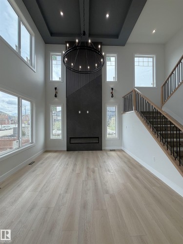 Two-story living area featuring a modern fireplace with dark paneling, a coffered ceiling with recessed lighting, and a large circular chandelier - 202 Edgewater Circle, Leduc, AB - Indoor Photo Showing Other Room