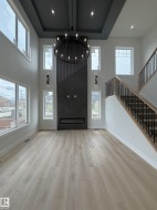 Two-story living area featuring a modern fireplace with dark paneling, a coffered ceiling with recessed lighting, and a large circular chandelier - 