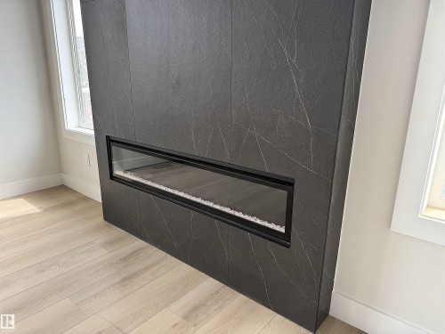 Contemporary fireplace with a dark stone-look surround and linear glass-enclosed firebox - 202 Edgewater Circle, Leduc, AB - Indoor Photo Showing Other Room With Fireplace