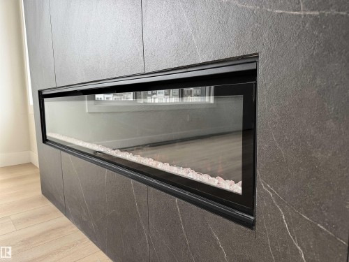 Contemporary linear fireplace with a black glass front, integrated into a dark stone-finish accent wall with subtle veining - 202 Edgewater Circle, Leduc, AB - Indoor Photo Showing Other Room
