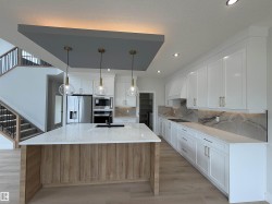 Modern kitchen featuring a large island with a light wood-finish base, a light-toned countertop, and three clear glass pendant lights - 