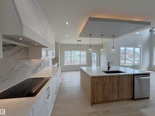 Contemporary kitchen featuring a large island with a dark sink and matte black faucet, integrated dishwasher, and three pendant lights - 202 Edgewater Circle, Leduc, AB - Indoor Photo Showing Kitchen With Upgraded Kitchen