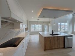Contemporary kitchen featuring a large island with a dark sink and matte black faucet, integrated dishwasher, and three pendant lights - 