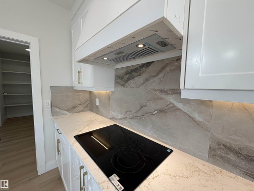 Modern kitchen featuring a sleek black induction cooktop, light-toned countertops with subtle veining, and a complementary gray tiled backsplash - 202 Edgewater Circle, Leduc, AB - Indoor Photo Showing Kitchen
