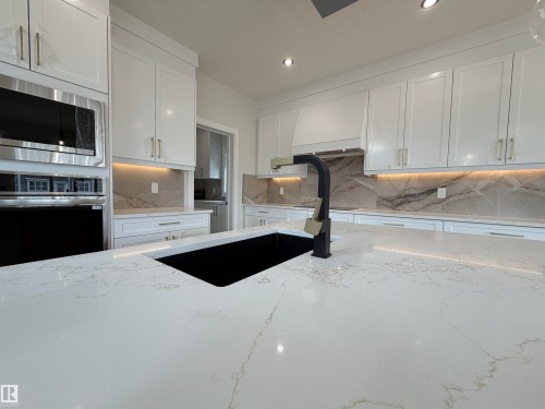 Kitchen featuring a large island with a black undermount sink and matte black faucet - 202 Edgewater Circle, Leduc, AB - Indoor Photo Showing Kitchen With Double Sink