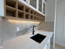 Built-in wet bar featuring a black undermount sink with a matte black faucet, light-toned countertop, and marble-look tile backsplash - 