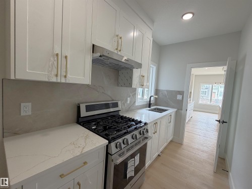 Contemporary kitchen featuring white shaker cabinetry with gold-tone hardware, stainless steel gas range, quartz countertops, and a coordinating full-height backsplash - 202 Edgewater Circle, Leduc, AB - Indoor Photo Showing Kitchen With Upgraded Kitchen