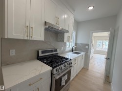 Contemporary kitchen featuring white shaker cabinetry with gold-tone hardware, stainless steel gas range, quartz countertops, and a coordinating full-height backsplash - 