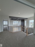 Upper-level landing featuring neutral carpeting, contemporary baluster railing, recessed lighting, and a coffered ceiling detail with an integrated chandelier - 