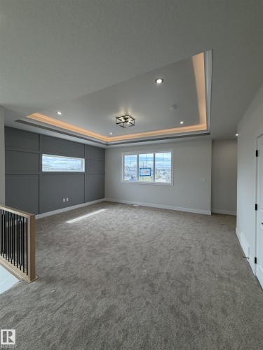 Spacious room featuring a tray ceiling with recessed lighting and cove illumination, gray accent wall with paneling, large windows, and neutral carpeting - 202 Edgewater Circle, Leduc, AB - Indoor Photo Showing Other Room