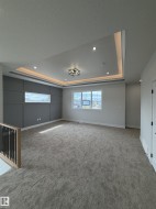 Spacious room featuring a tray ceiling with recessed lighting and cove illumination, gray accent wall with paneling, large windows, and neutral carpeting - 