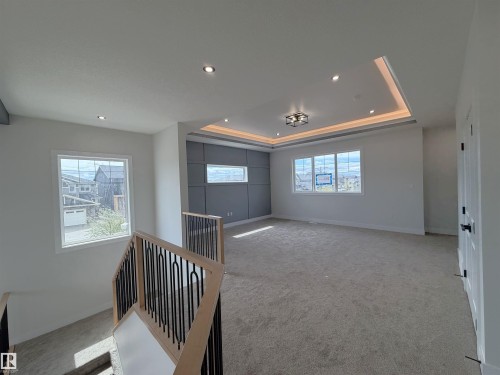 Carpeted upper-level space featuring a tray ceiling with recessed and cove lighting, multiple windows, and a paneled accent wall - 202 Edgewater Circle, Leduc, AB - Indoor Photo Showing Other Room