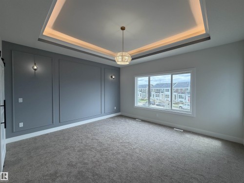 Contemporary room featuring a tray ceiling with accent lighting, a modern spherical chandelier, and wall sconces - 202 Edgewater Circle, Leduc, AB - Indoor Photo Showing Other Room