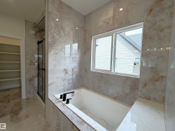 Contemporary bathroom featuring an integrated soaking tub with a matte black faucet, surrounded by large format porcelain wall tiles - 